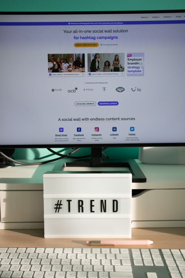 about-us-01 A clean and modern desk setup with a lightbox displaying #TREND and a computer monitor showing a social wall solution.